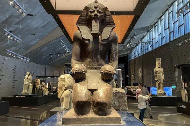 Image is of the female Pharaoh Hatshepsut kneeling and offering Nu vases, part of the collection at the Grand Egyptian Museum.